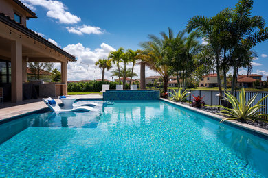 Large modern backyard custom-shaped infinity pool in Miami with a hot tub and natural stone pavers.