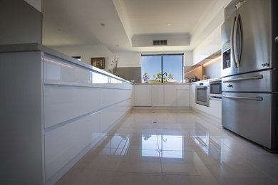 Large modern u-shaped eat-in kitchen in Perth with an undermount sink, flat-panel cabinets, white cabinets, quartz benchtops, metallic splashback, glass sheet splashback, stainless steel appliances, porcelain floors, a peninsula, beige floor and grey benchtop.