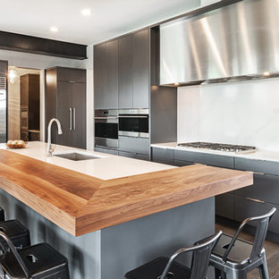 Inspiration pour une grande arrière-cuisine design en L avec un évier 2 bacs, un placard à porte plane, des portes de placard grises, un plan de travail en quartz modifié, une crédence blanche, une crédence en dalle de pierre, un électroménager en acier inoxydable, un sol en bois brun, un îlot central, un sol marron et un plan de travail blanc.