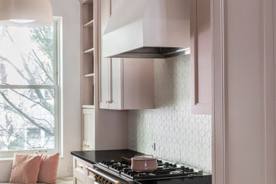 Small transitional galley light wood floor enclosed kitchen photo in New York with an undermount sink, recessed-panel cabinets, pink cabinets, soapstone countertops, white backsplash, ceramic backsplash, paneled appliances and black countertops