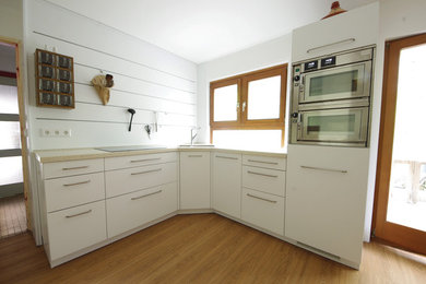 Geschlossene, Einzeilige, Große Moderne Küche ohne Insel mit Doppelwaschbecken, flächenbündigen Schrankfronten, braunen Schränken, Mineralwerkstoff-Arbeitsplatte, Küchenrückwand in Weiß, Rückwand aus Holz, Küchengeräten aus Edelstahl, braunem Holzboden und braunem Boden in Frankfurt am Main