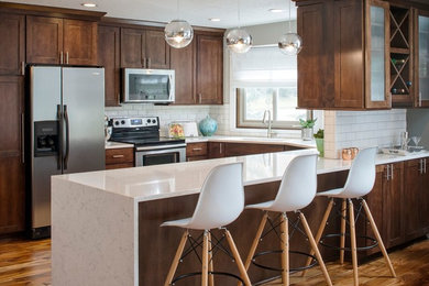 Inspiration for a mid-sized transitional l-shaped medium tone wood floor and brown floor kitchen remodel in Omaha with shaker cabinets, brown cabinets, quartz countertops, white backsplash, subway tile backsplash, stainless steel appliances and a peninsula