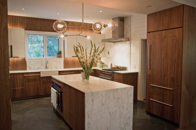 Example of a large transitional u-shaped ceramic tile and black floor kitchen pantry design in Other with a farmhouse sink, flat-panel cabinets, medium tone wood cabinets, marble countertops, white backsplash, marble backsplash, paneled appliances, an island and white countertops