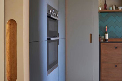 This is an example of a medium sized midcentury grey and black l-shaped enclosed kitchen in Edinburgh with a built-in sink, flat-panel cabinets, black cabinets, wood worktops, green splashback, cement tile splashback, cork flooring, no island, white floors, black worktops, a coffered ceiling and feature lighting.