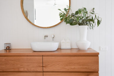 サンシャインコーストにあるビーチスタイルのおしゃれな浴室 (家具調キャビネット、淡色木目調キャビネット、白いタイル、白い壁、木製洗面台、洗面台1つ、フローティング洗面台) の写真