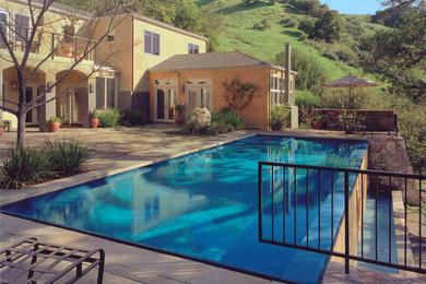 This is an example of a mid-sized traditional backyard rectangular infinity pool in Orange County with a water feature and natural stone pavers.