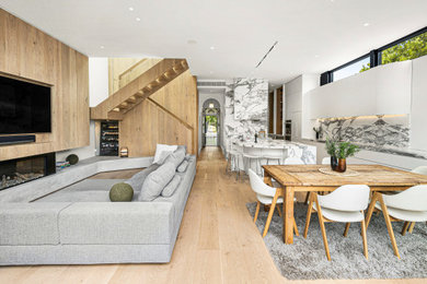 Mid-sized modern open concept living room in Melbourne with white walls, light hardwood floors, a standard fireplace, a wood fireplace surround, a wall-mounted tv and wood walls.