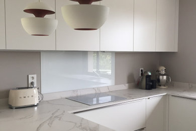 This is an example of a large modern u-shaped open plan kitchen in Toulouse with an integrated sink, beaded inset cabinets, white cabinets, quartzite benchtops, white splashback, glass tile splashback, stainless steel appliances, light hardwood floors, white benchtop, with island and grey floor.