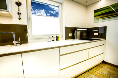This is an example of a contemporary galley separate kitchen in Stuttgart with white cabinets, marble benchtops, black splashback, glass sheet splashback, black appliances and no island.