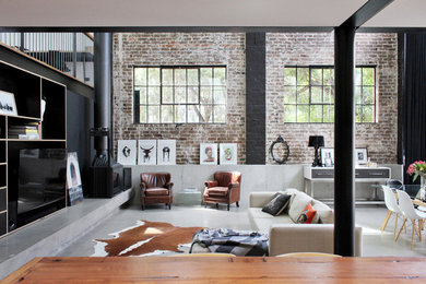 Photo of an expansive industrial loft-style living room in Sydney with black walls, concrete floors, a corner fireplace, a concrete fireplace surround and a built-in media wall.