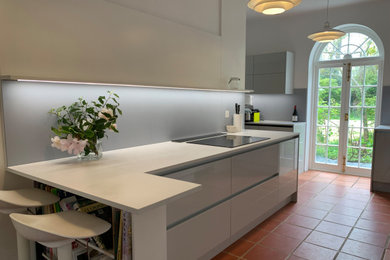 Design ideas for a large traditional grey and white galley open plan kitchen in Hampshire with a double-bowl sink, flat-panel cabinets, grey cabinets, composite countertops, blue splashback, porcelain splashback, integrated appliances, terracotta flooring, orange floors, white worktops and feature lighting.