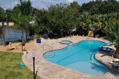 This is an example of a large traditional backyard custom-shaped natural pool in Jacksonville with a water slide and natural stone pavers.