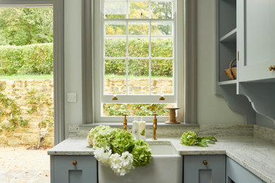 Utility room - small traditional slate floor and gray floor utility room idea in Wiltshire with a farmhouse sink, recessed-panel cabinets, blue cabinets, marble countertops, white backsplash, marble backsplash, white walls and white countertops