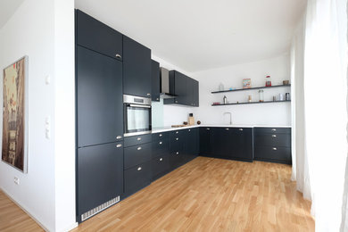 Offene, Mittelgroße Moderne Küche ohne Insel in L-Form mit Einbauwaschbecken, flächenbündigen Schrankfronten, blauen Schränken, Küchenrückwand in Blau, Glasrückwand, Küchengeräten aus Edelstahl, braunem Holzboden und braunem Boden in Köln