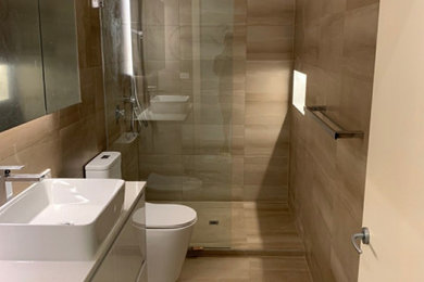Design ideas for a large contemporary 3/4 bathroom in Melbourne with flat-panel cabinets, white cabinets, a corner shower, a two-piece toilet, beige tile, porcelain tile, beige walls, porcelain floors, an integrated sink, solid surface benchtops, beige floor, an open shower, white benchtops, a niche, a single vanity and a freestanding vanity.