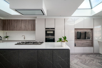 This is an example of a large contemporary l-shaped kitchen/diner in London with quartz worktops, engineered quartz splashback, integrated appliances, an island, white worktops and feature lighting.