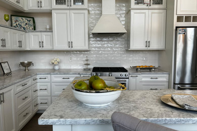 Example of a mid-sized l-shaped brown floor kitchen design in New York with an undermount sink, white cabinets, white backsplash, stainless steel appliances and an island