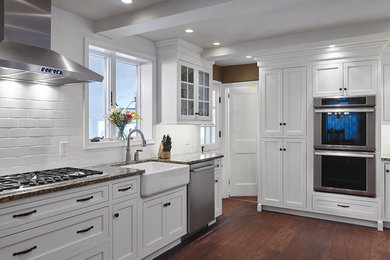 Example of a large transitional u-shaped dark wood floor and brown floor enclosed kitchen design in Philadelphia with a farmhouse sink, shaker cabinets, yellow cabinets, granite countertops, white backsplash, subway tile backsplash, stainless steel appliances and no island