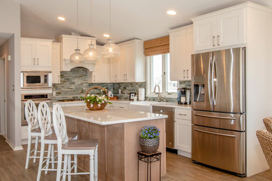 Open concept kitchen - mid-sized coastal l-shaped vinyl floor and brown floor open concept kitchen idea in New York with a farmhouse sink, shaker cabinets, white cabinets, quartzite countertops, multicolored backsplash, glass tile backsplash, stainless steel appliances, an island and white countertops