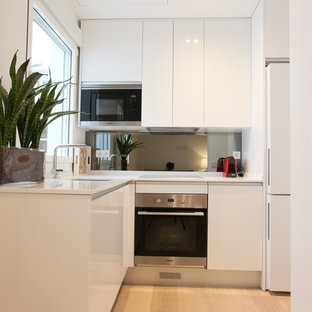 На фото: маленькая угловая кухня-гостиная в скандинавском стиле с врезной раковиной, плоскими фасадами, белыми фасадами, столешницей из кварцевого композита, серым фартуком, фартуком с окном, техникой из нержавеющей стали, светлым паркетным полом, бежевым полом и белой столешницей без острова с
