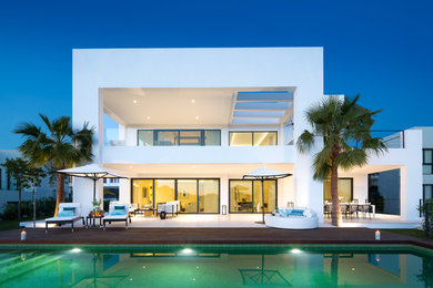 This is an example of a contemporary two-storey stucco white house exterior in Other with a flat roof.