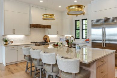 Kitchen - contemporary l-shaped light wood floor and beige floor kitchen idea in Raleigh with an undermount sink, flat-panel cabinets, white cabinets, white backsplash, stainless steel appliances, an island and beige countertops