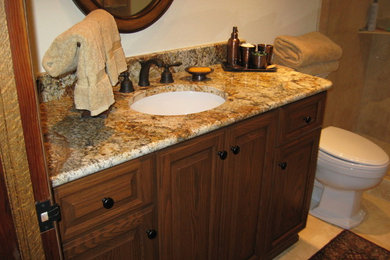 Mid-sized elegant porcelain tile porcelain tile and beige floor bathroom photo in Orange County with raised-panel cabinets, dark wood cabinets, a two-piece toilet, beige walls, an undermount sink, granite countertops and brown countertops