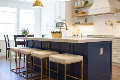 Kitchen - galley medium tone wood floor kitchen idea in Orange County with an undermount sink, shaker cabinets, white cabinets, quartz countertops, white backsplash, subway tile backsplash, stainless steel appliances, an island and white countertops