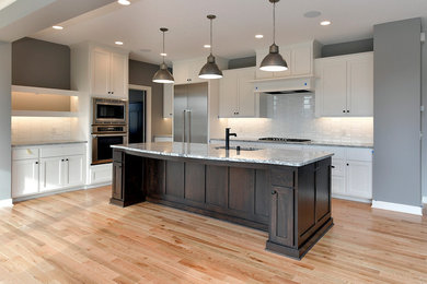 This is an example of a large transitional l-shaped eat-in kitchen in Minneapolis with a single-bowl sink, shaker cabinets, white cabinets, granite benchtops, white splashback, ceramic splashback, stainless steel appliances, light hardwood floors, with island and brown floor.