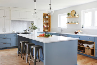 Design ideas for a transitional l-shaped kitchen in Toronto with an undermount sink, shaker cabinets, blue cabinets, white splashback, mosaic tile splashback, stainless steel appliances, medium hardwood floors, with island, brown floor and white benchtop.