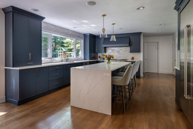 Inspiration for a large transitional l-shaped medium tone wood floor open concept kitchen remodel in New York with an undermount sink, recessed-panel cabinets, blue cabinets, quartz countertops, ceramic backsplash, stainless steel appliances and an island