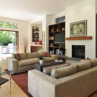 Exempel på ett modernt allrum med öppen planlösning, med ett bibliotek, en standard öppen spis, vita väggar, mellanmörkt trägolv, en spiselkrans i gips och en inbyggd mediavägg