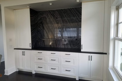 Design ideas for a mid-sized arts and crafts single-wall home bar in Seattle with no sink, shaker cabinets, white cabinets, marble benchtops, black splashback, marble splashback, dark hardwood floors, brown floor and black benchtop.