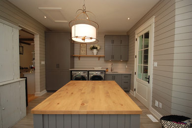 Example of a large transitional porcelain tile utility room design in Ottawa with an undermount sink, shaker cabinets, gray cabinets, wood countertops, gray walls and a side-by-side washer/dryer