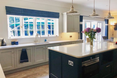 Photo of a mid-sized contemporary galley eat-in kitchen in Surrey with a drop-in sink, shaker cabinets, blue cabinets, blue splashback, glass sheet splashback, stainless steel appliances, with island and brown floor.