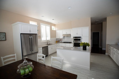 This is an example of a mid-sized traditional l-shaped eat-in kitchen in Sacramento with an undermount sink, white cabinets, white splashback, stainless steel appliances, with island, multi-coloured floor, multi-coloured benchtop, recessed-panel cabinets and granite benchtops.