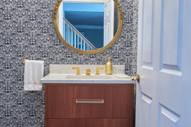 Photo of a small contemporary powder room in Philadelphia with flat-panel cabinets, medium wood cabinets, a two-piece toilet, grey walls, medium hardwood floors, an undermount sink, engineered quartz benchtops, brown floor, white benchtops, a floating vanity and wallpaper.