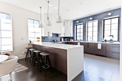 This is an example of a large contemporary l-shaped eat-in kitchen in New York with an undermount sink, flat-panel cabinets, dark wood cabinets, solid surface benchtops, grey splashback, matchstick tile splashback, stainless steel appliances, a peninsula, grey floor and porcelain floors.