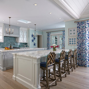 Inspiration pour une cuisine ouverte linéaire marine avec des portes de placard blanches, un plan de travail en marbre, une crédence bleue, une crédence en mosaïque, un sol en bois clair, 2 îlots et un placard avec porte à panneau encastré.