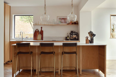 This is an example of a large modern l-shaped open plan kitchen in Sussex with a built-in sink, flat-panel cabinets, medium wood cabinets, stainless steel appliances, medium hardwood flooring, an island, brown floors and white worktops.