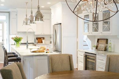 Mid-sized transitional galley medium tone wood floor and brown floor eat-in kitchen photo in St Louis with an undermount sink, shaker cabinets, white cabinets, marble countertops, white backsplash, ceramic backsplash, stainless steel appliances and an island