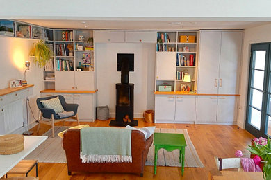 This is an example of a medium sized contemporary open plan living room in Cornwall with white walls, medium hardwood flooring, a wood burning stove and a concealed tv.