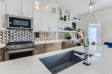Example of a large eclectic galley light wood floor open concept kitchen design in Denver with a single-bowl sink, shaker cabinets, white cabinets, quartz countertops, blue backsplash, glass tile backsplash, stainless steel appliances, a peninsula and white countertops
