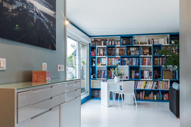 Cette image montre un grand salon design ouvert avec une bibliothèque ou un coin lecture, un mur bleu, parquet peint, une cheminée standard, un manteau de cheminée en métal, un téléviseur encastré et un sol blanc.