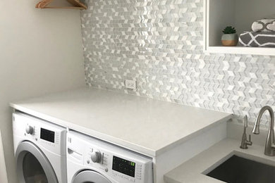Mid-sized single-wall ceramic tile and gray floor laundry room photo in Chicago with an utility sink, shaker cabinets, white cabinets, quartz countertops, gray walls, a side-by-side washer/dryer and white countertops
