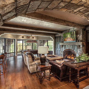 Foto di un grande soggiorno mediterraneo aperto con pareti beige, pavimento in legno massello medio, camino classico, cornice del camino in pietra, TV a parete, pavimento multicolore e sala giochi