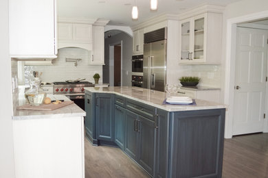 Example of a mid-sized classic medium tone wood floor and brown floor enclosed kitchen design in Cleveland with an undermount sink, recessed-panel cabinets, white cabinets, quartzite countertops, white backsplash, porcelain backsplash, stainless steel appliances, an island and gray countertops