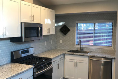 Example of a small transitional l-shaped vinyl floor, brown floor and vaulted ceiling open concept kitchen design with a drop-in sink, shaker cabinets, white cabinets, granite countertops, gray backsplash, subway tile backsplash, stainless steel appliances, no island and white countertops