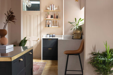 Design ideas for a medium sized midcentury galley kitchen/diner in Manchester with a belfast sink, flat-panel cabinets, black cabinets, quartz worktops, metallic splashback, metal splashback, integrated appliances, light hardwood flooring, no island and white worktops.
