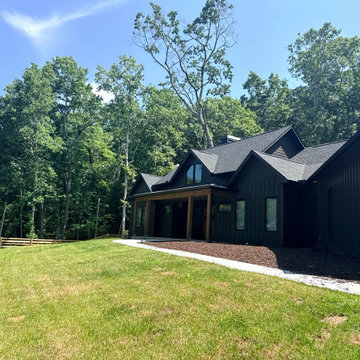 Wide Exterior View of a Dark Modern Farmhouse on a Sloped Wooded Lot